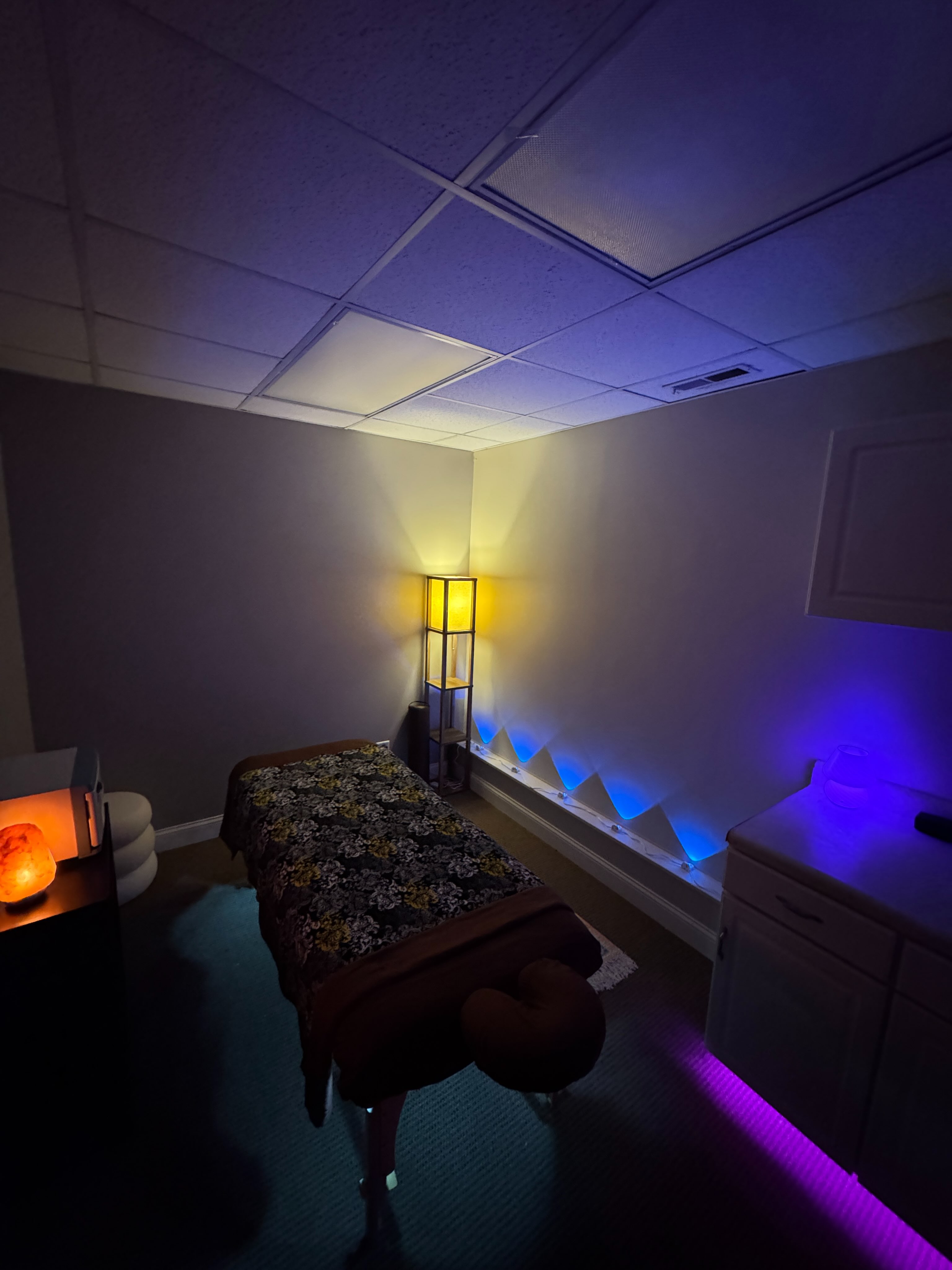 Alexander’s Crystal Lake massage room with a massage table, warm salt lamp, and violet and blue ambient lighting
